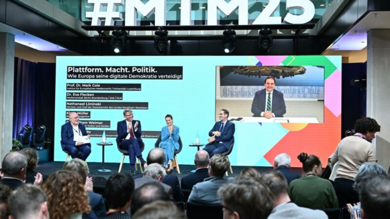 Podiumsdiskussion mit Experten und Politikern zum Thema 'Plattform. Macht. Politik. Wie Europa seine digitale Demokratie verteidigt'. Im Hintergrund eine große Leinwand mit Livestream, im Vordergrund ein interessiertes Publikum.