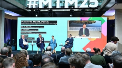 Podiumsdiskussion mit Experten und Politikern zum Thema 'Plattform. Macht. Politik. Wie Europa seine digitale Demokratie verteidigt'. Im Hintergrund eine große Leinwand mit Livestream, im Vordergrund ein interessiertes Publikum.